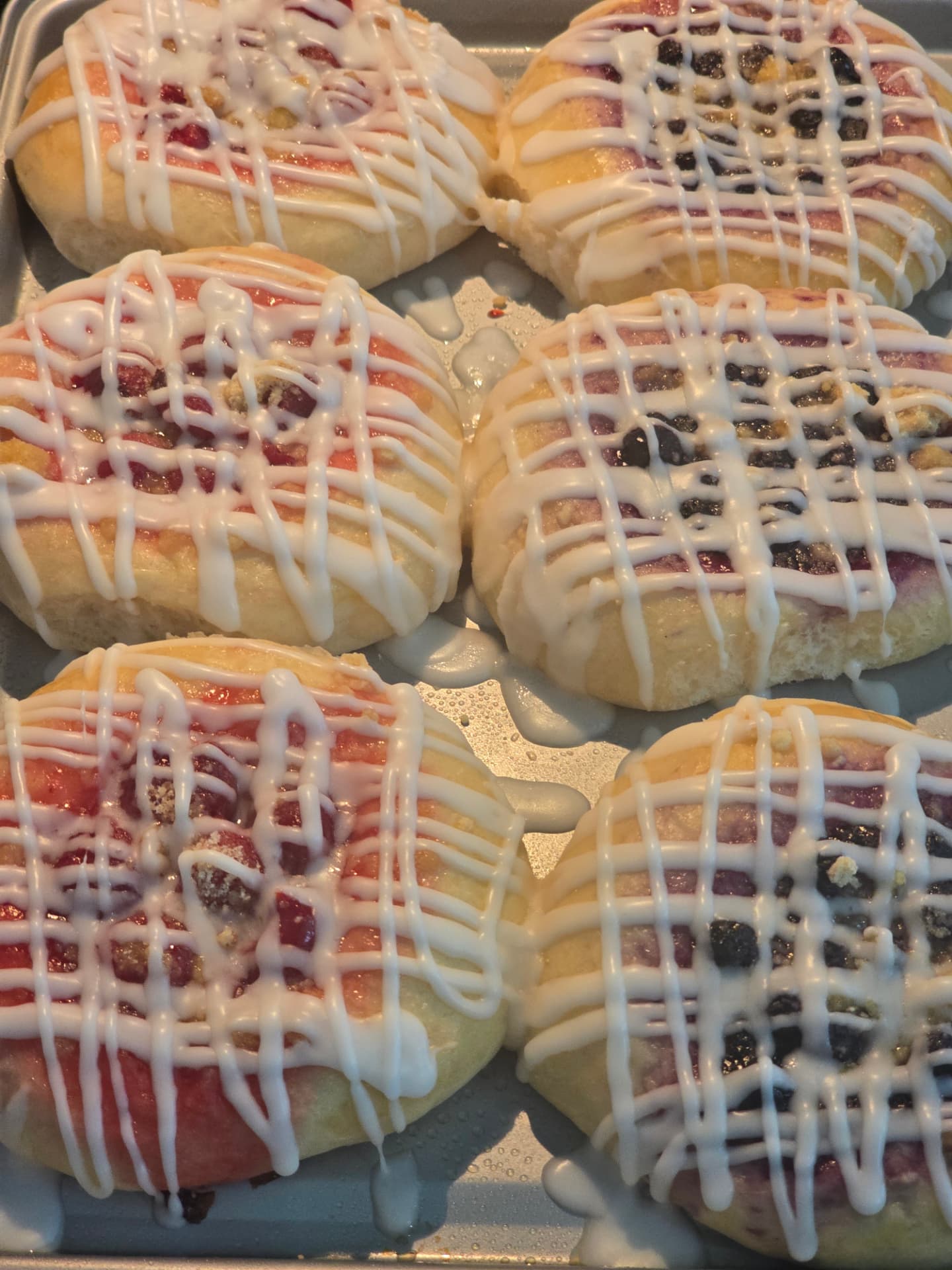 Assorted fruit kolaches with sweet icing drizzle arranged on a baking tray