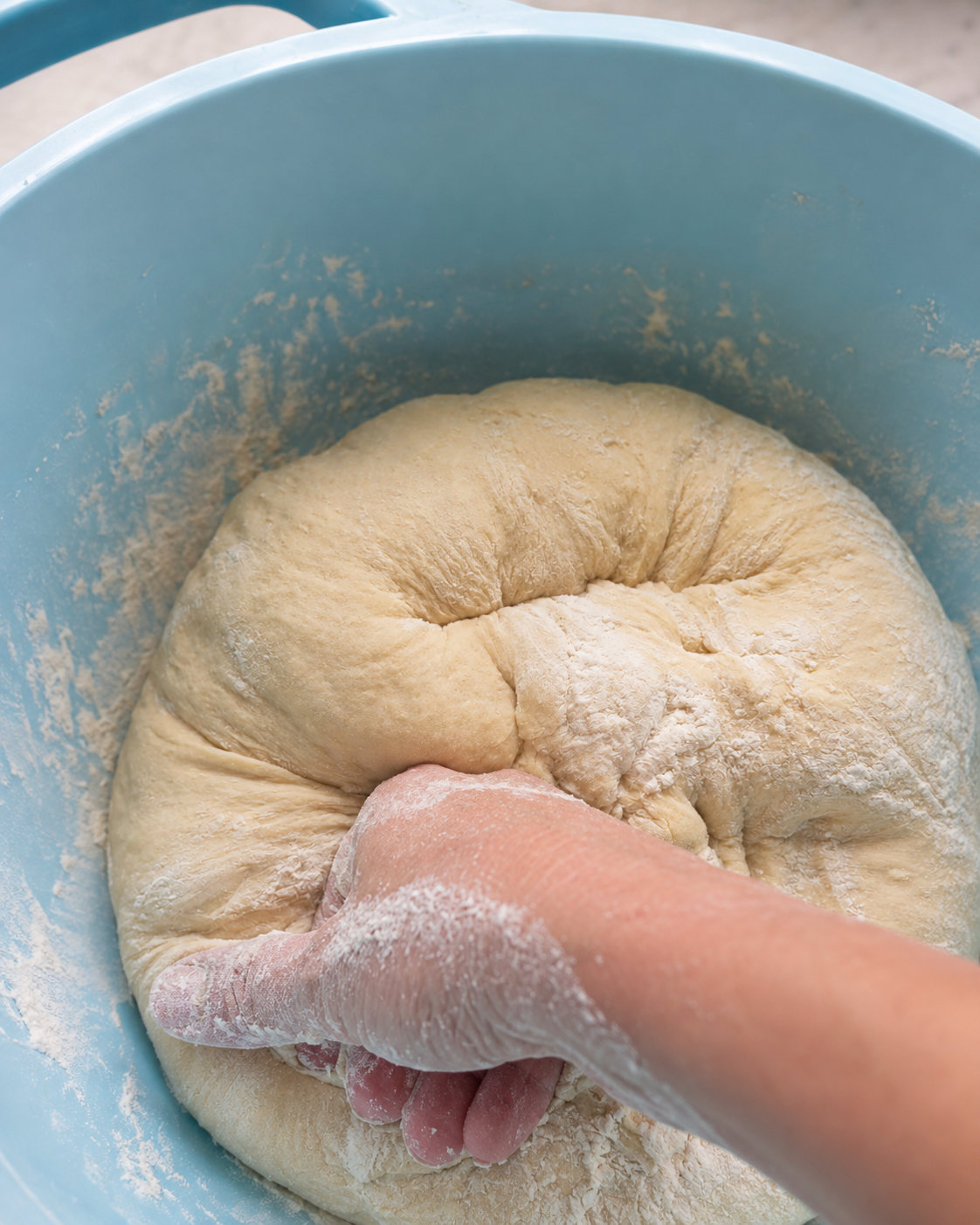 A baker's hand pressing into a mound of floured dough