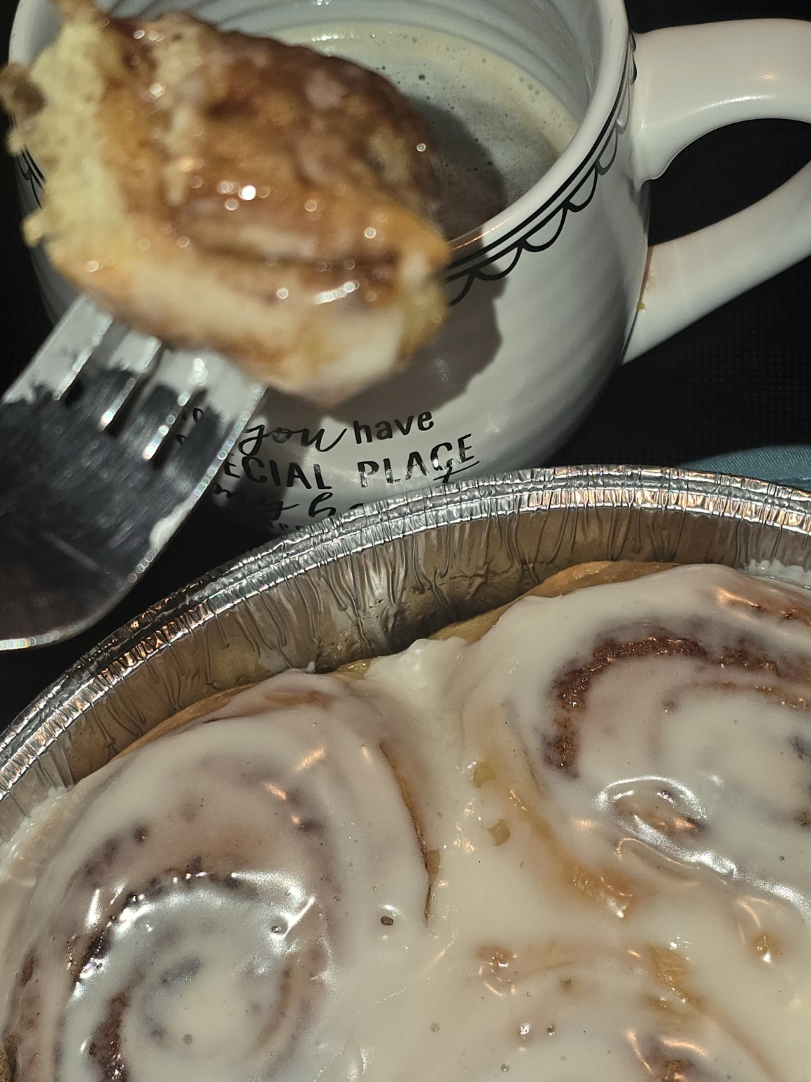 A forkful of iced cinnamon roll beside a mug of coffee